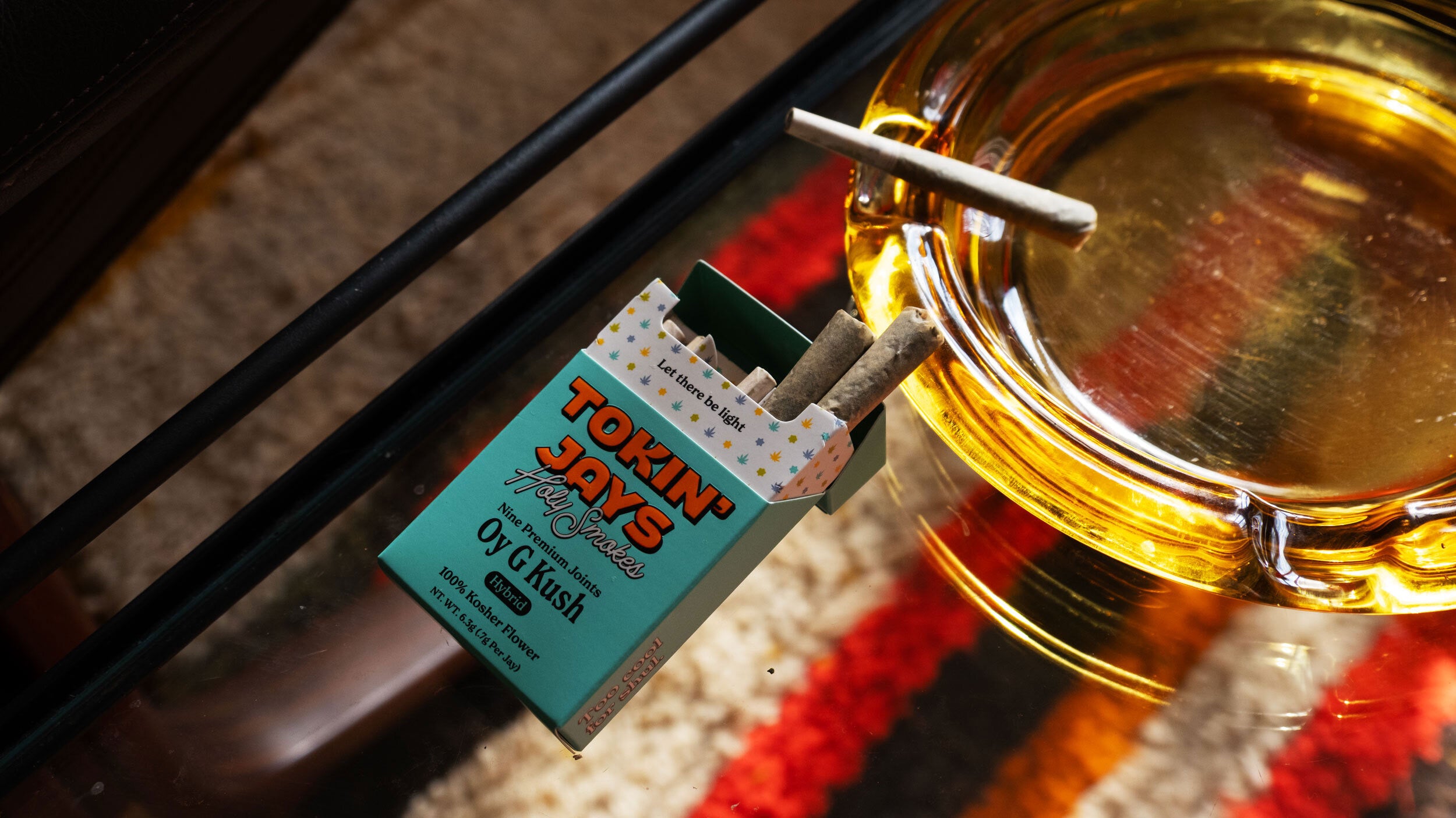 pack of Toxin Jay's Oy G Kush joints next to a glass of amber liquid.