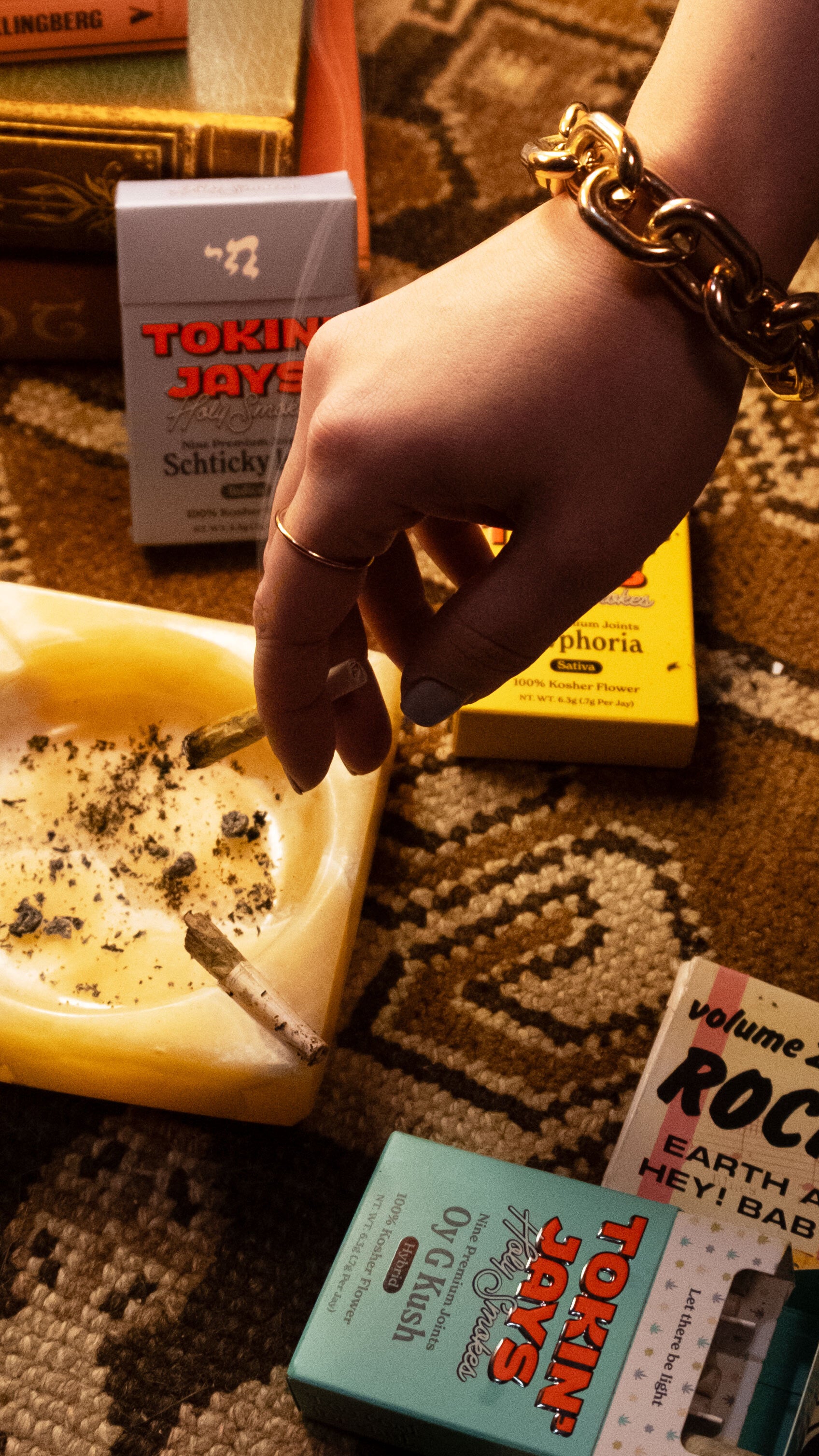 Hand holding a joint with various products and tokin jay packaging in the background on a textured surface.