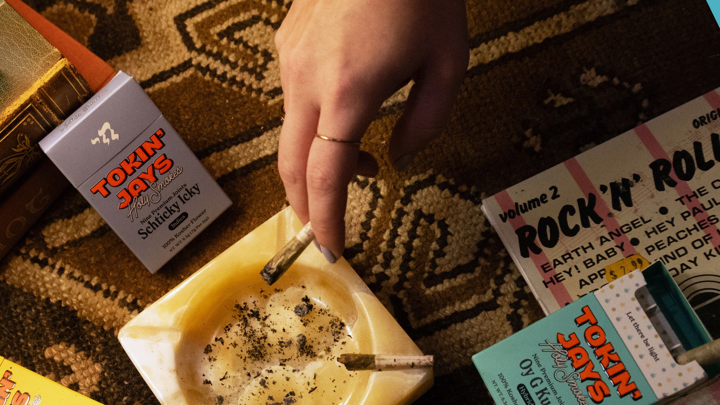 Hand holding a cigarette above an ashtray with 'Tokin' Jays' products around