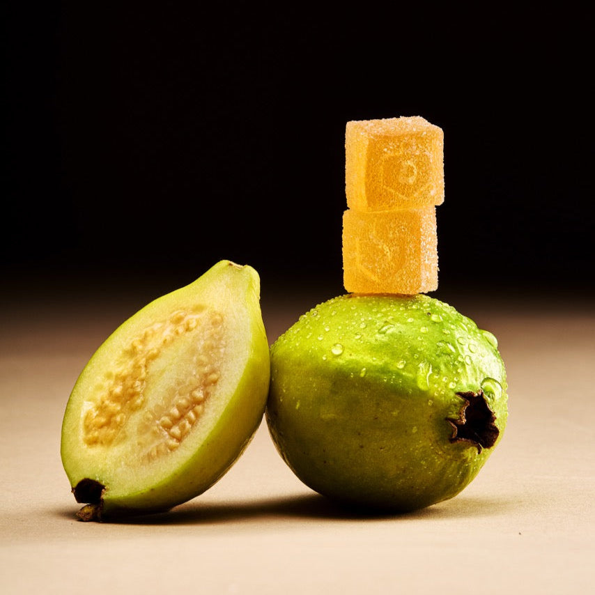Green guava fruit with a cut section and two tokin chew gummies on a dark background