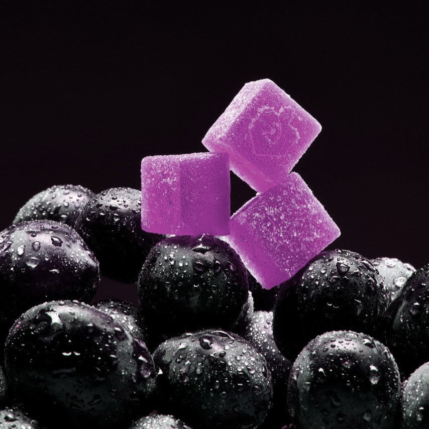 Purple gummies on wet grapes against a black background