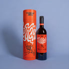 A bottle of Tokin' Jew Fruit of the Vine red wine stands next to its tall orange cylindrical packaging tube on a light blue-gray studio background.
