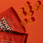 Two orange 'Tokin' Chews' packages with THC gummies on an orange background