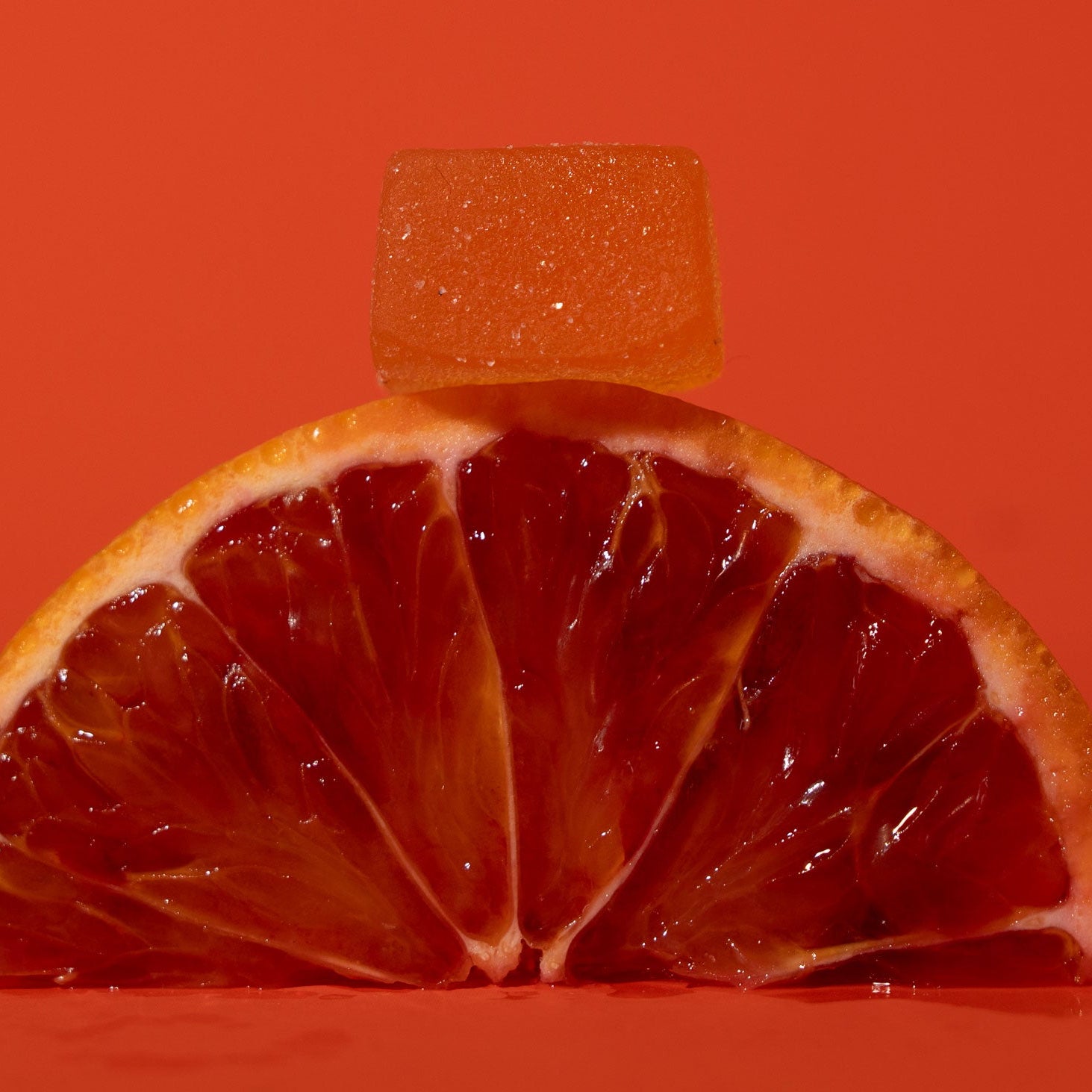 Sliced blood orange with a gummy on an orange background