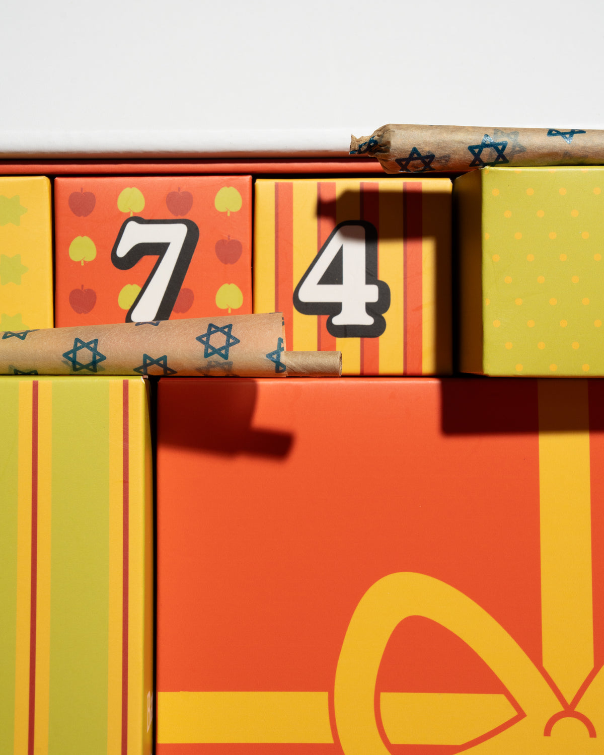 A close-up of colorful gift boxes with wrapped cigars resting across them. The boxes are bright orange, yellow, and green with decorative patterns, and the numbers 7 and 4 are printed on the front.