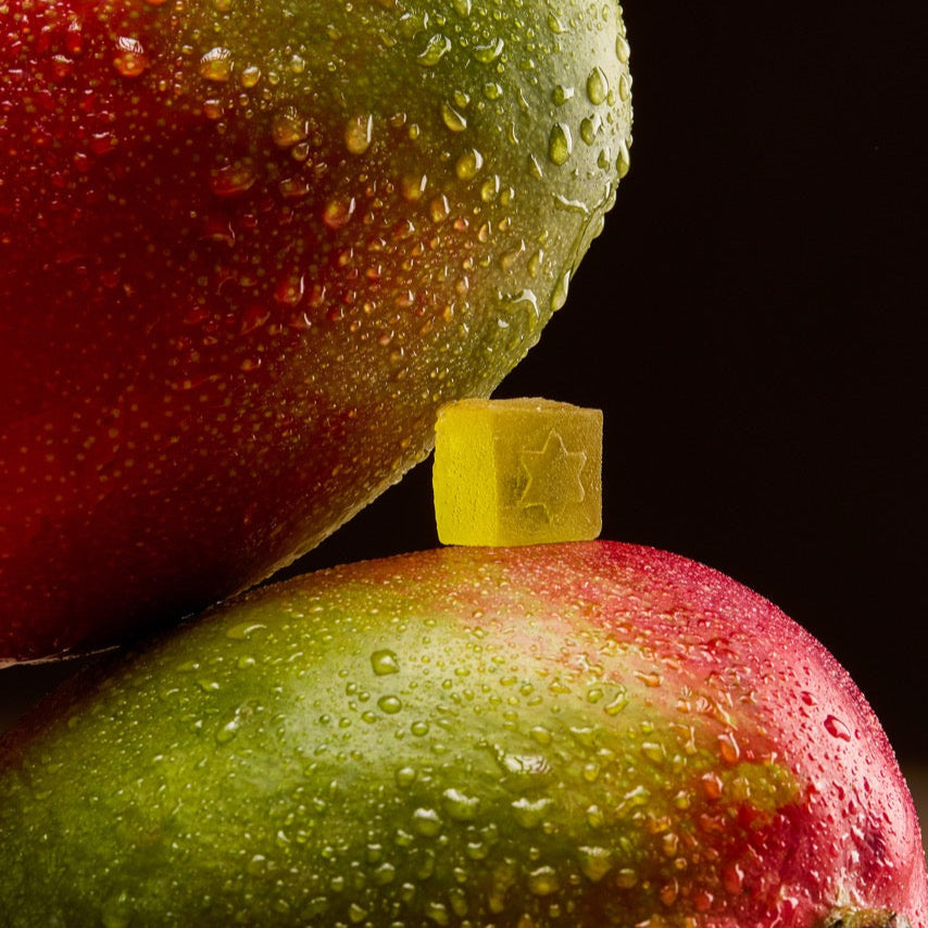 Two mangoes and a gummy with water droplets on a black background