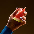 Hand holding a slice of watermelon with a watermelon gummy on a dark background