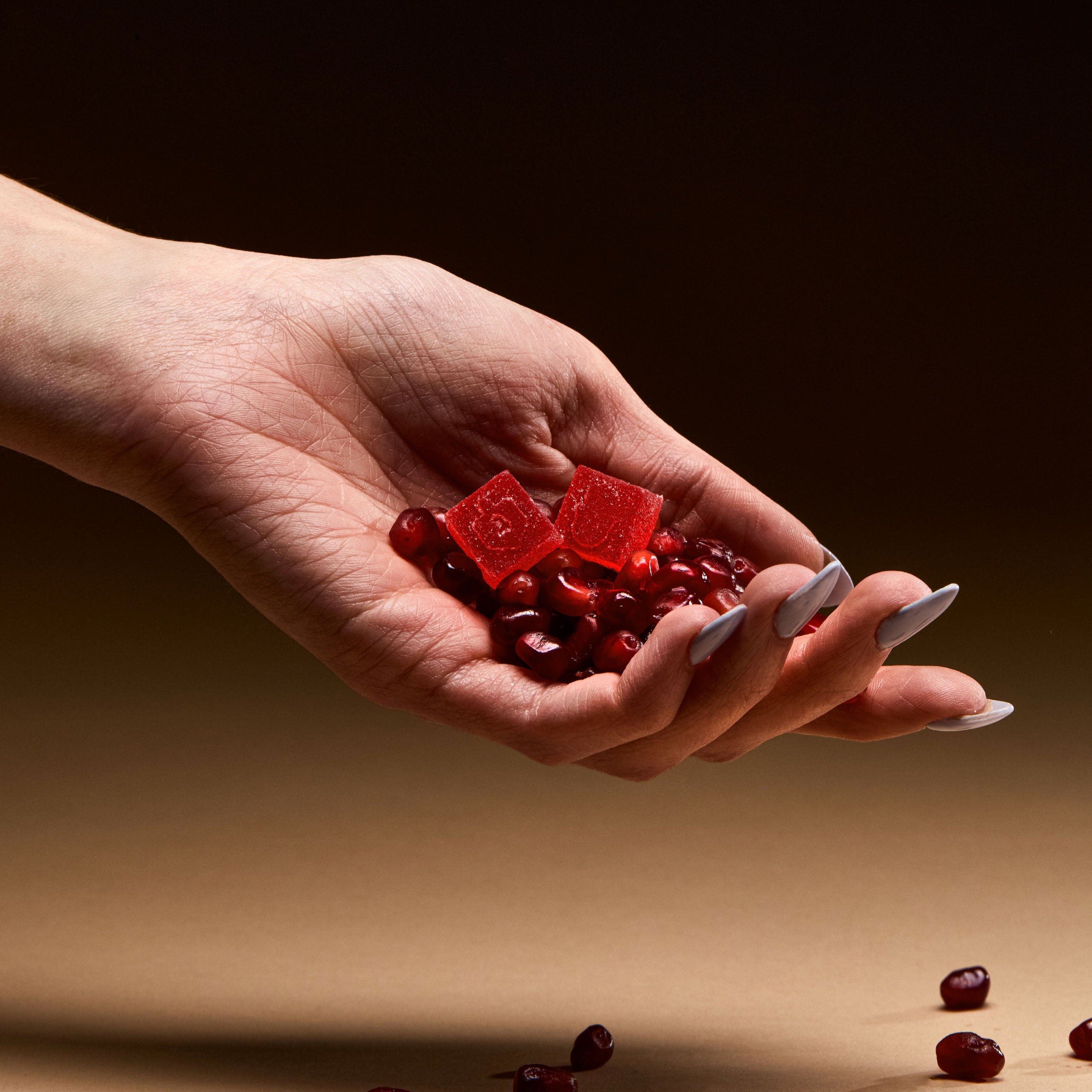 hand holding pomegranate seeds and 2 pomegranate gummies 