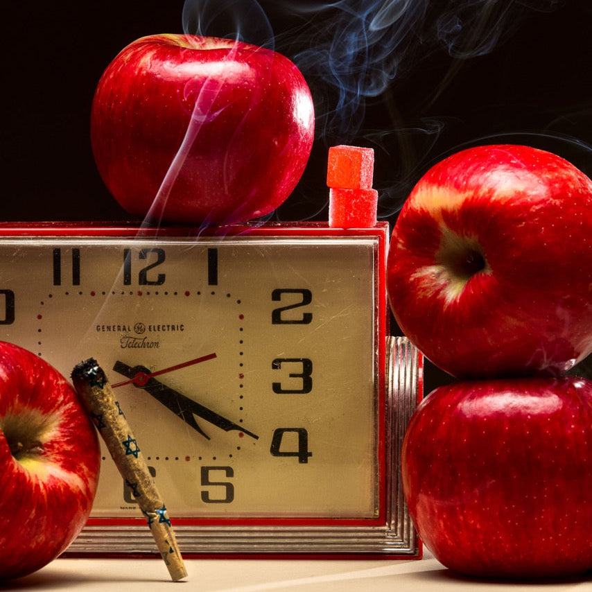 Vintage clock with red apples and a lit cigarette on a dark background