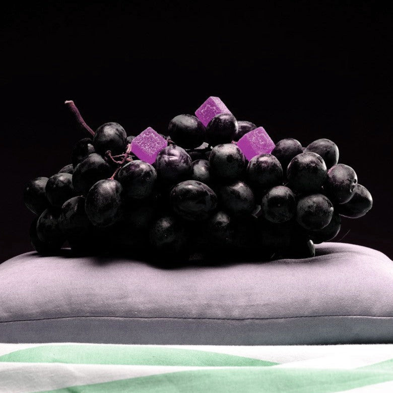Bunch of grapes with purple gummies on a gray pillow against a black background