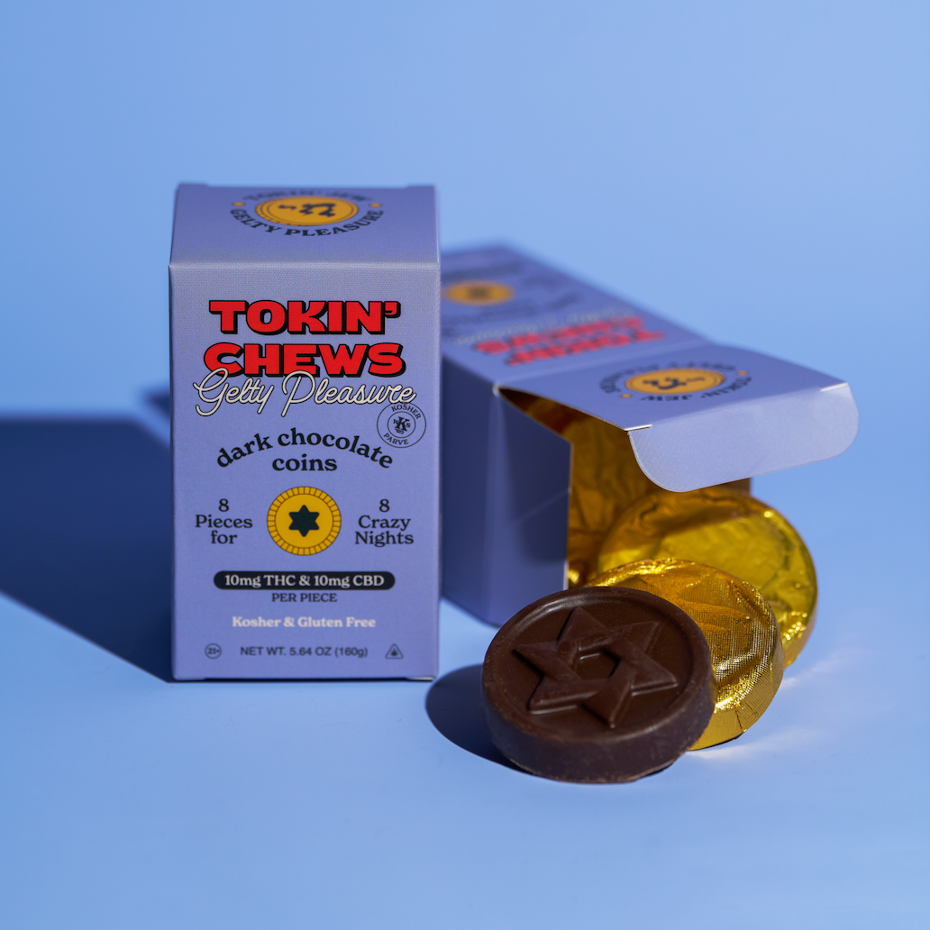 Tokin Chews Dark Chocolate coins in a light blue box with a gold foil-wrapped coin and a dark chocolate coin in front, set against a solid blue background.