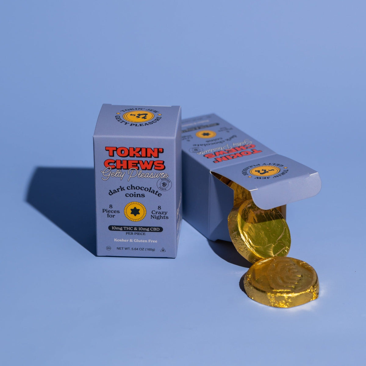 A box of Tokin' Chews dark chocolate chew treats sits on a light blue studio background, with one open box and several gold-wrapped round chews beside it.