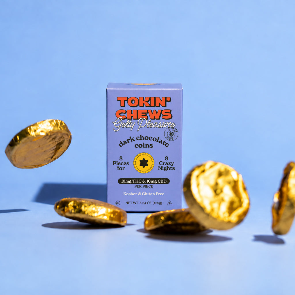 A box of Tokin' Chews Gold Edition dark chocolate coins stands on a light blue background with several gold foil-wrapped round chocolate coins floating around it.