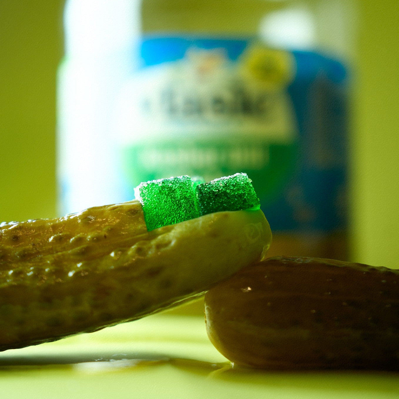 Jar of pickles with a pickle gummy on a yellow-green background