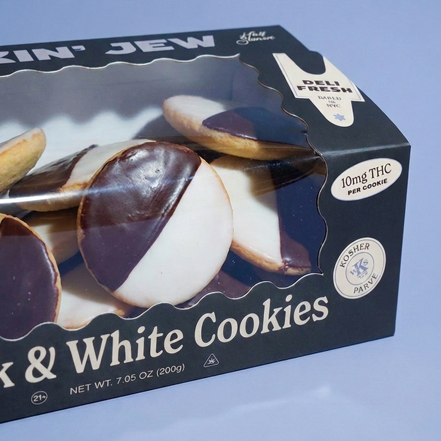 A boxed pack of chocolate-dipped and white-frosted cookies on a light blue background. The black box has a clear window showing several round cookies with dark chocolate halves and white frosting, plus text including 'Black & White Cookies,' 'Delhi Fresh,' '10mg THC per cookie,' and 'Kosher Passed.